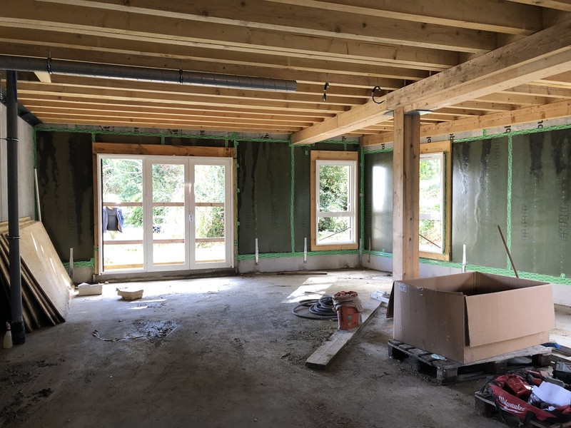 vue de l'intérieur d'un appartement. Poutre apparentes au plafond, pare vapeur vert sur les murs. Les menuiseries sont posées. Sur le sol on voit les affaires du chantier.